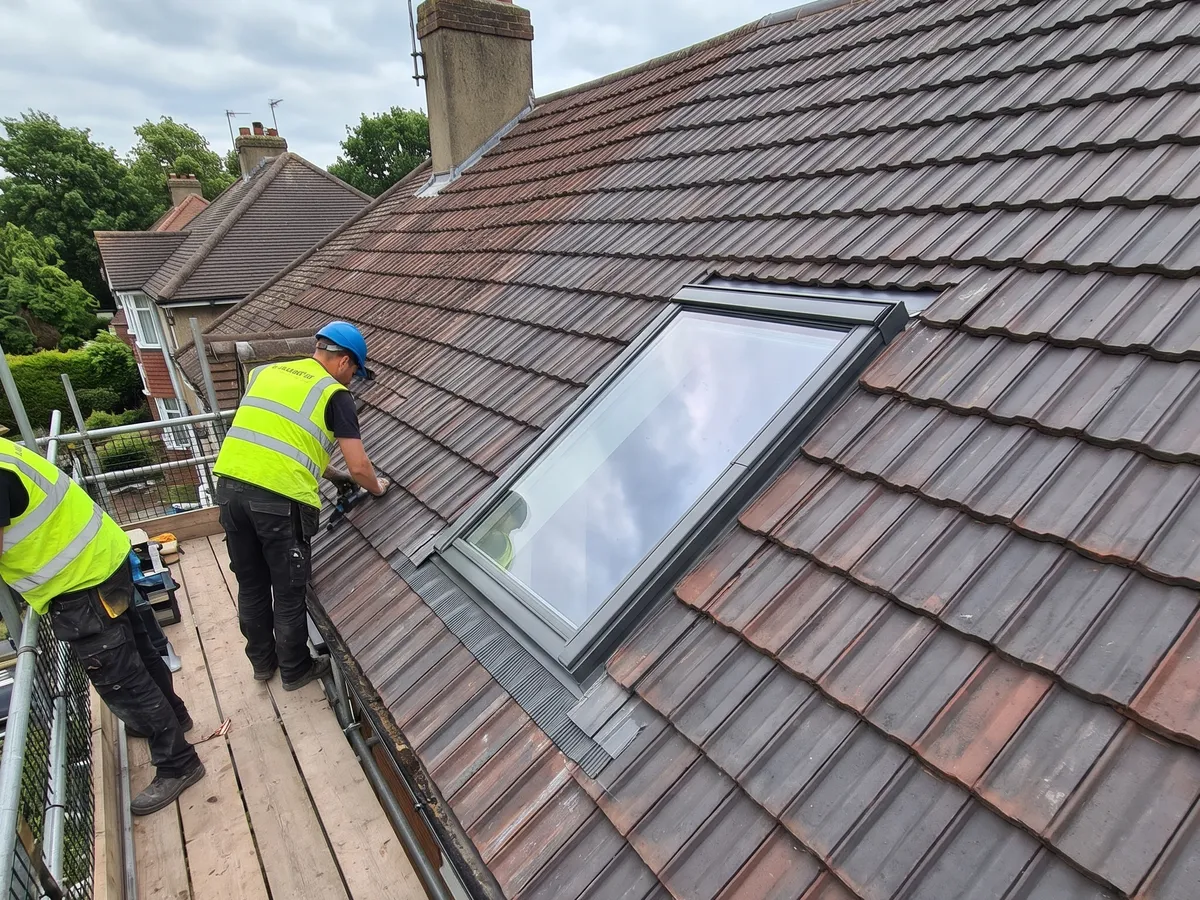 Roofers fitting a new Velux roof window into a tiled roof